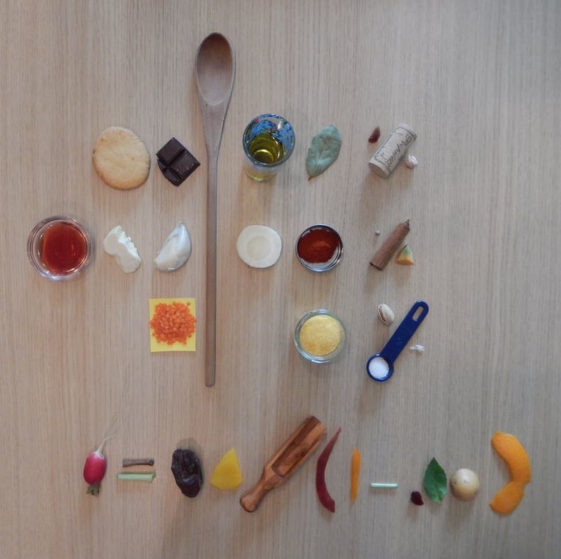 A variety of cooking ingredients arranged on a wooden surface, including spices, oils, and vegetables, with a wooden spoon in the center.